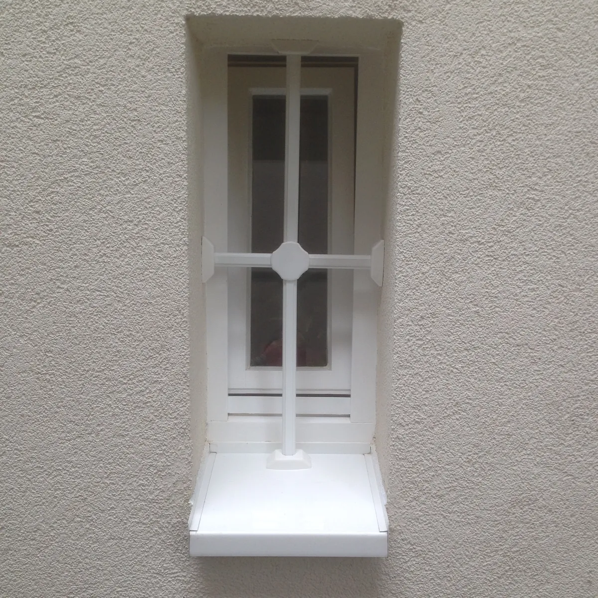 Weißes Fenstergitter vor einem schmalen Kellerfenster