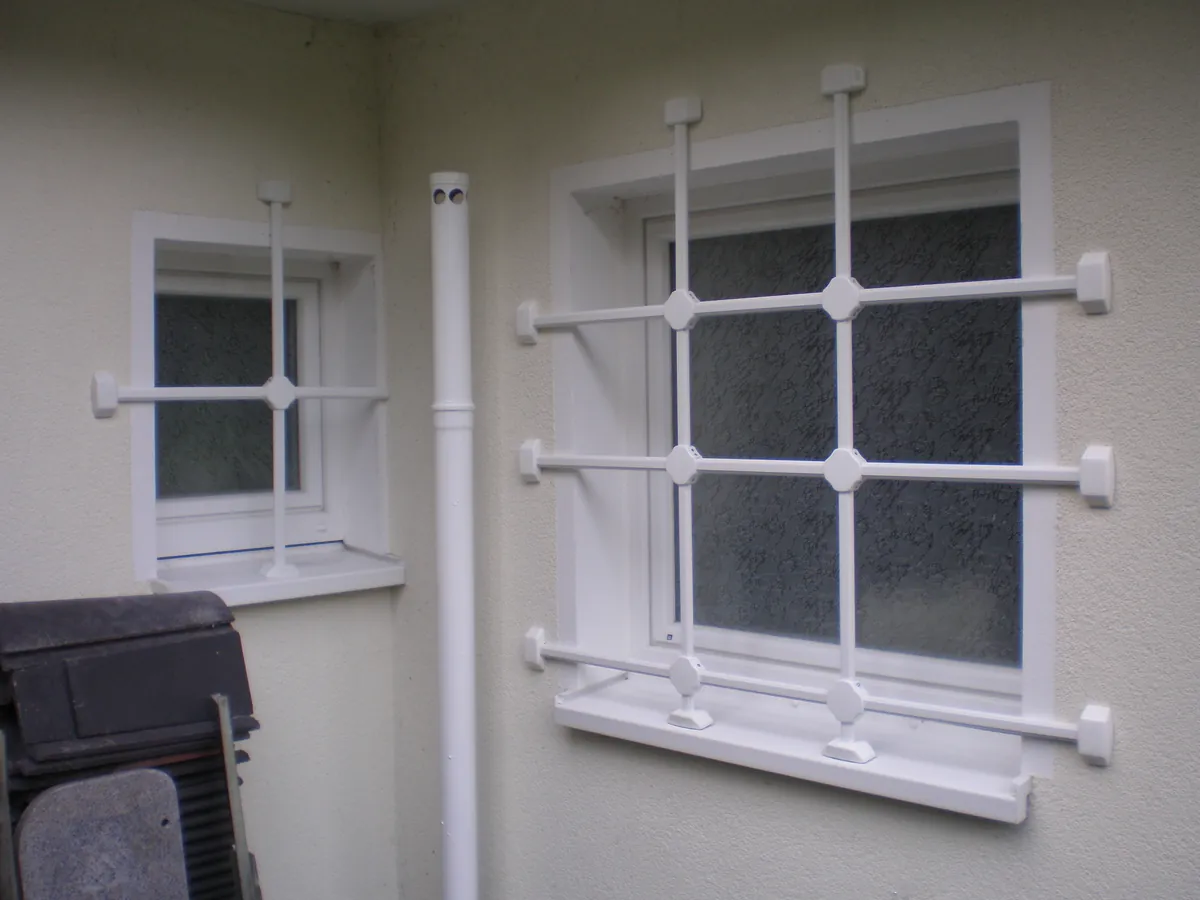 Weiße Fenstergitter vor zwei Fenstern an einer Hauswand