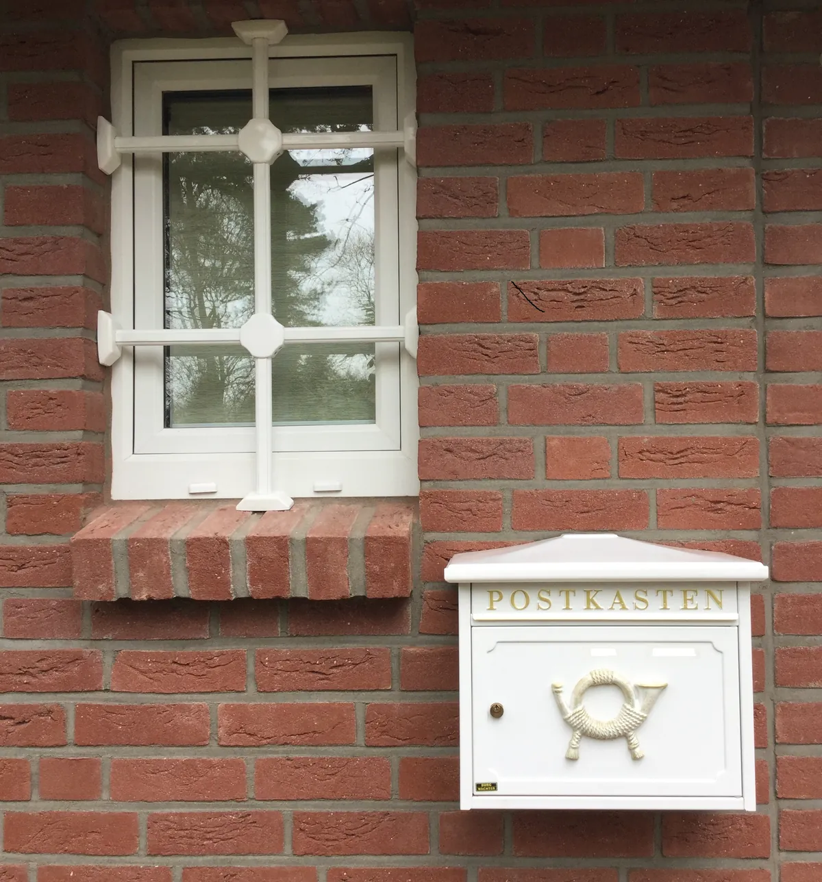 Fenster in Backsteinwand mit weißem Gitter über einem Briefkasten