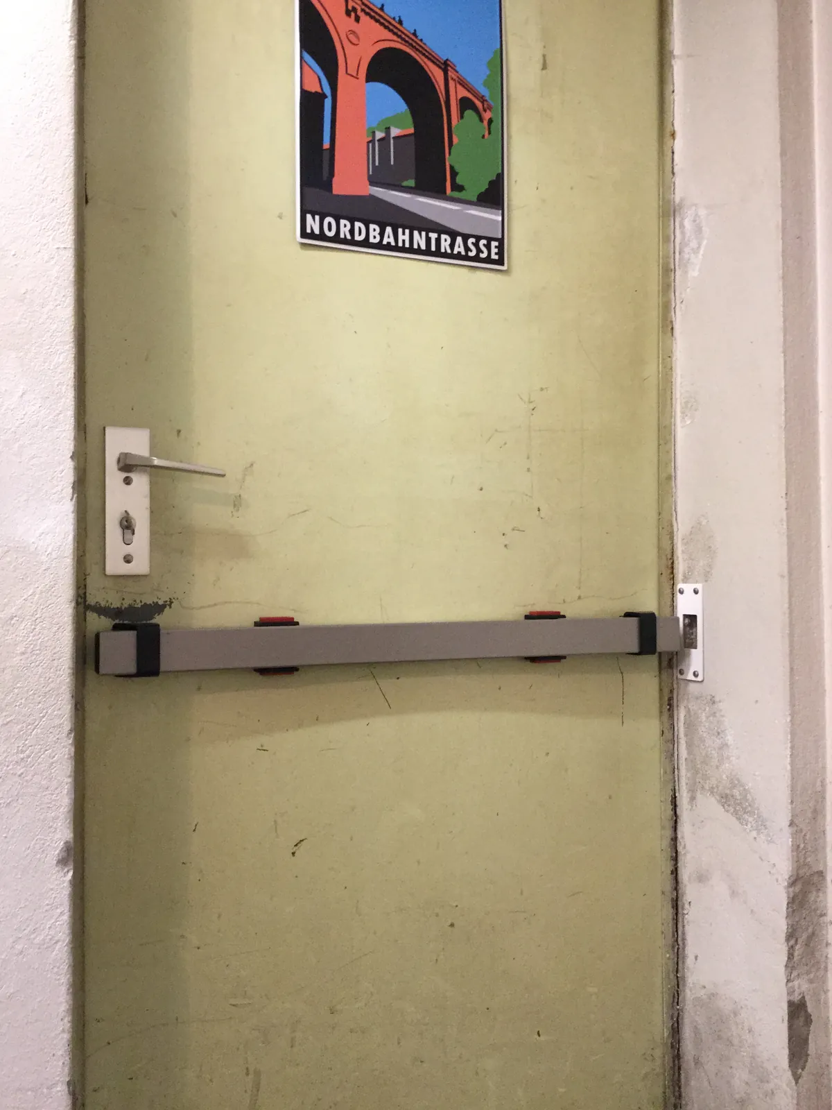 Tür mit dunklem Panzerriegel unter einem Plakat